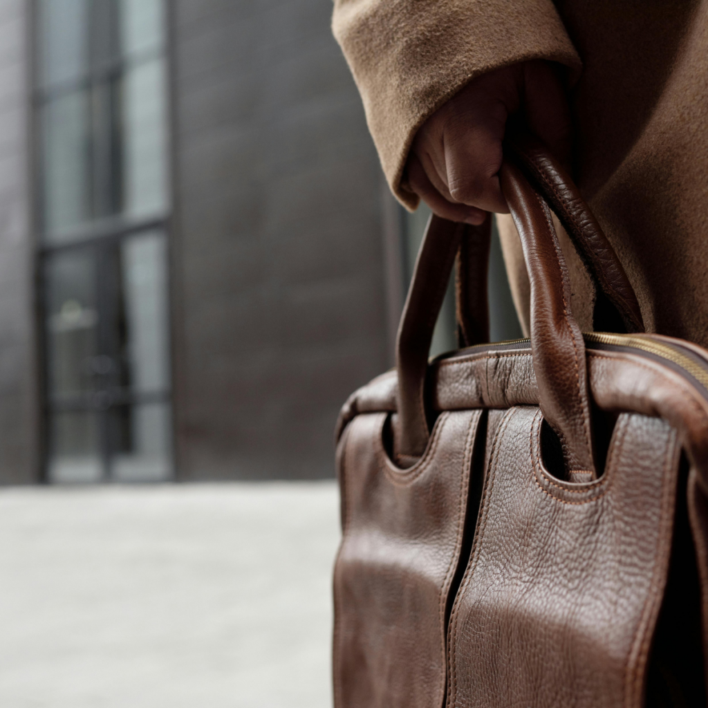 Hand einer Frau im beigen Wollmantel, die eine braune Ledertasche am Henkel hält